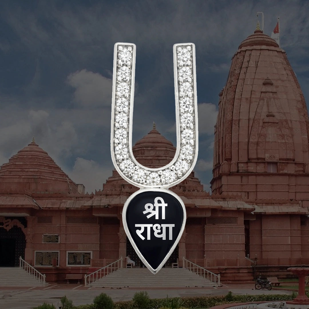 Diamond-studded silver U-shaped pendant with black enamel Shri Radha charm displayed against Hindu temple background