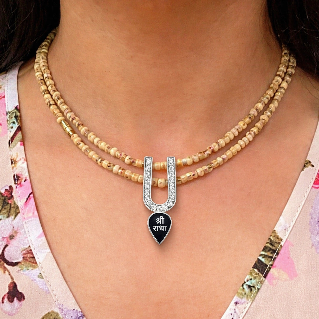 Woman wearing diamond silver U-shaped pendant with black Shri Radha charm on layered gold bead necklace